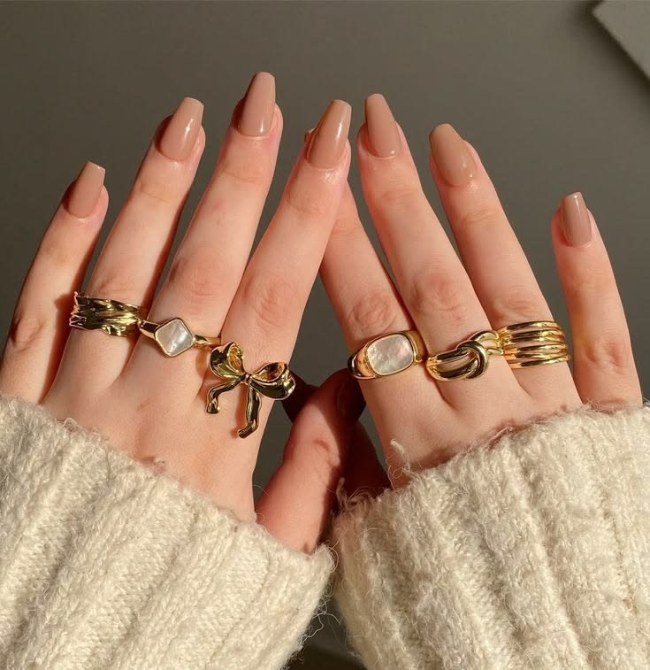 Soft nude almond nails styled with gold rings for a clean, elegant look